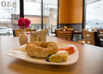 Plate of simit with garnishes on a cafe table, small vase with pink carnation in the background