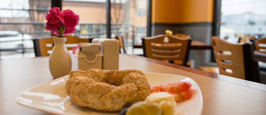 Plate of simit with garnishes on a cafe table, small vase with pink carnation in the background