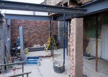 Construction site with steel beams and brickwork, scaffolding and tools visible, under renovation in progress