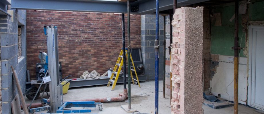 Construction site with steel beams and brickwork, scaffolding and tools visible, under renovation in progress
