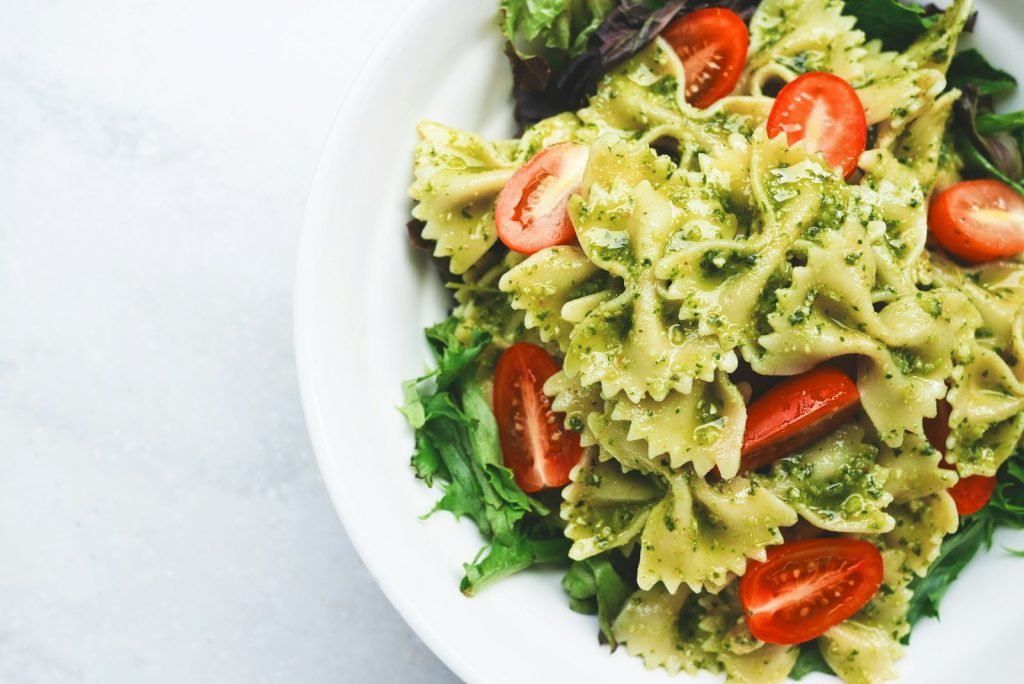 Fresh bowtie pasta salad with pesto, cherry tomatoes, and greens in white bowl