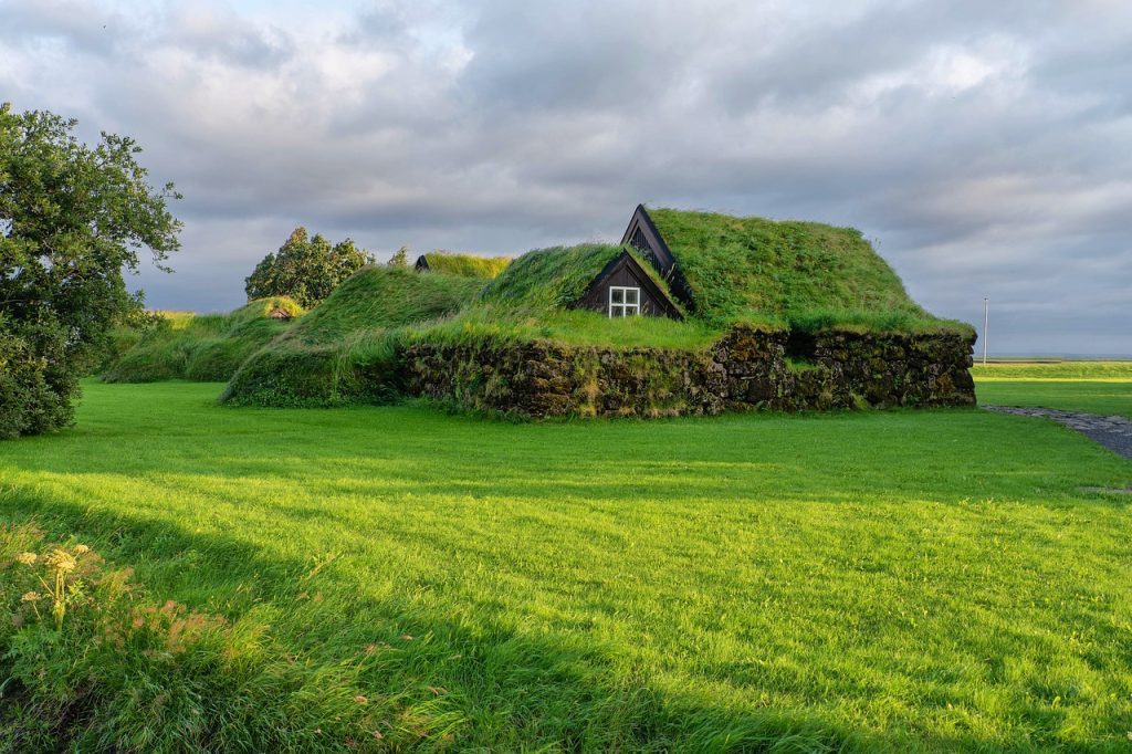 Green roofed sod house in lush Icelandic countryside under a cloudy sky