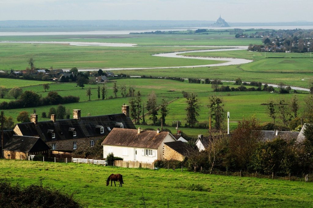 Idyllic countryside village with a grazing horse and distant view of Mont Saint-Michel and winding river landscape