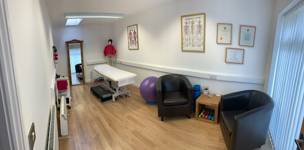 Chiropractic clinic room with treatment table, chairs, fitness equipment, and anatomical charts on the wall