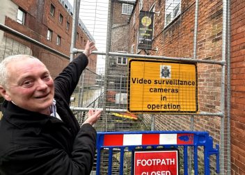 Man indicating surveillance sign and closed footpath in urban alleyway setting
