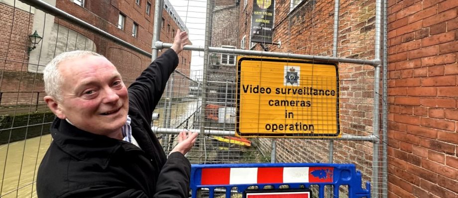 Man indicating surveillance sign and closed footpath in urban alleyway setting