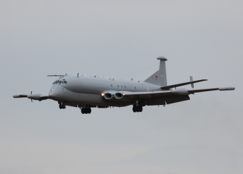 Grey military aircraft in mid-air flight against a cloudy sky background