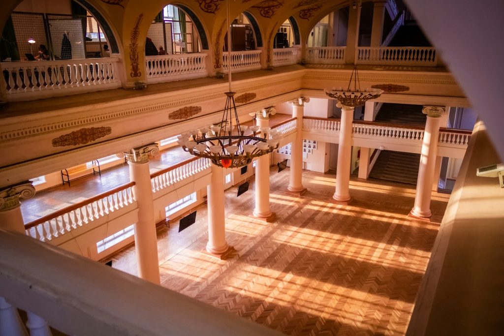 Historic interior with grand staircase and decorative columns bathed in warm sunlight, featuring intricate ceiling designs