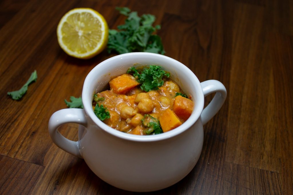 Creamy sweet potato and chickpea stew in a white bowl, garnished with fresh kale, lemon half in background