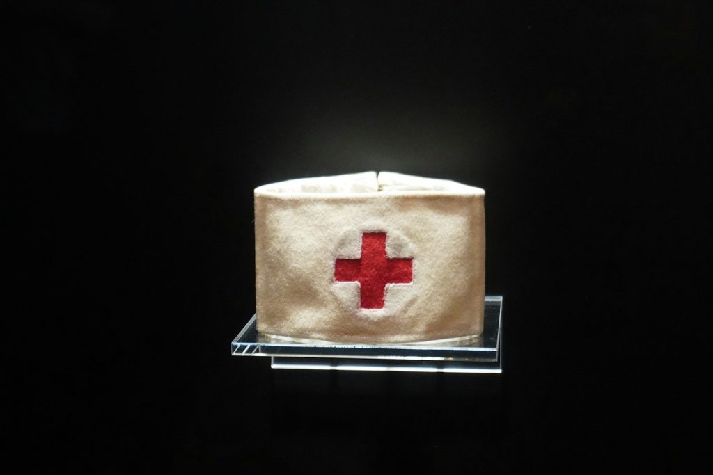 White nurse's hat with red cross emblem on black background, symbolising healthcare and medical profession