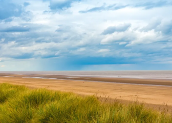 Expansive sandy beach with grassy dunes and a dramatic cloudy sky, peaceful coastal scene in the UK