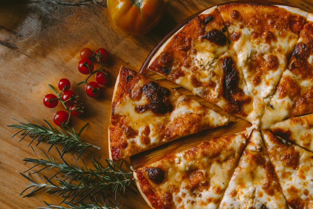 Delicious cheese pizza with cherry tomatoes and fresh rosemary on a rustic wooden table surface