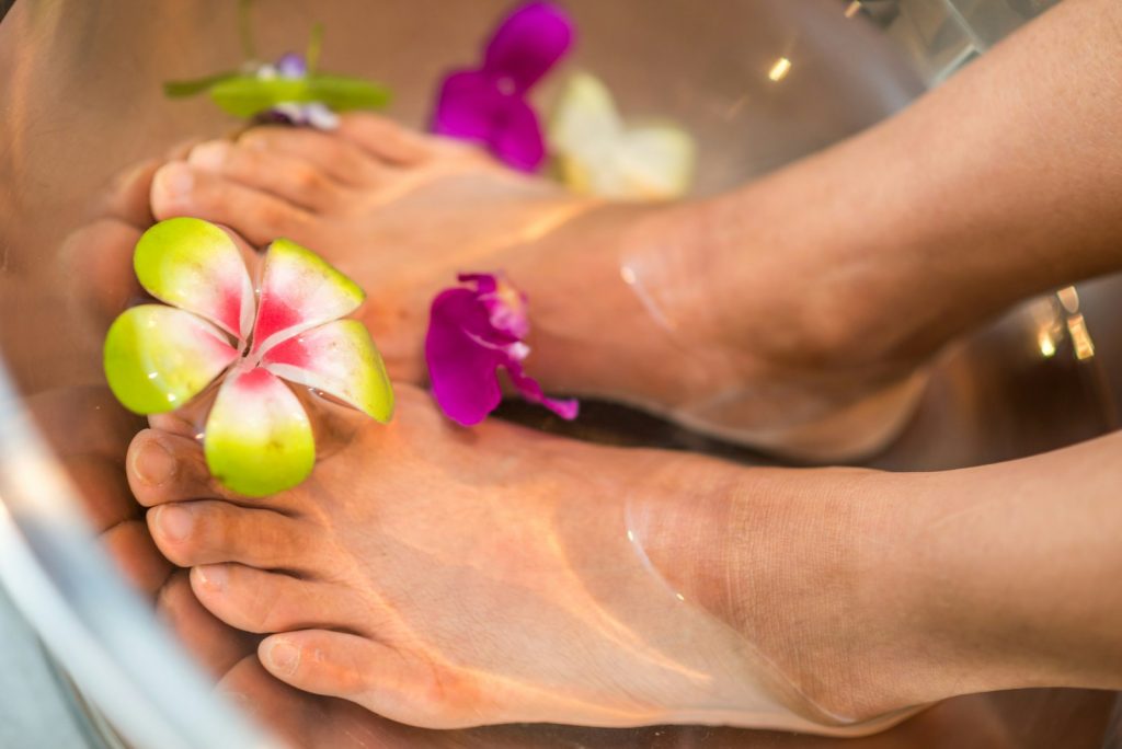 Feet soaking in water with floating colourful flower petals for a relaxing spa treatment experience