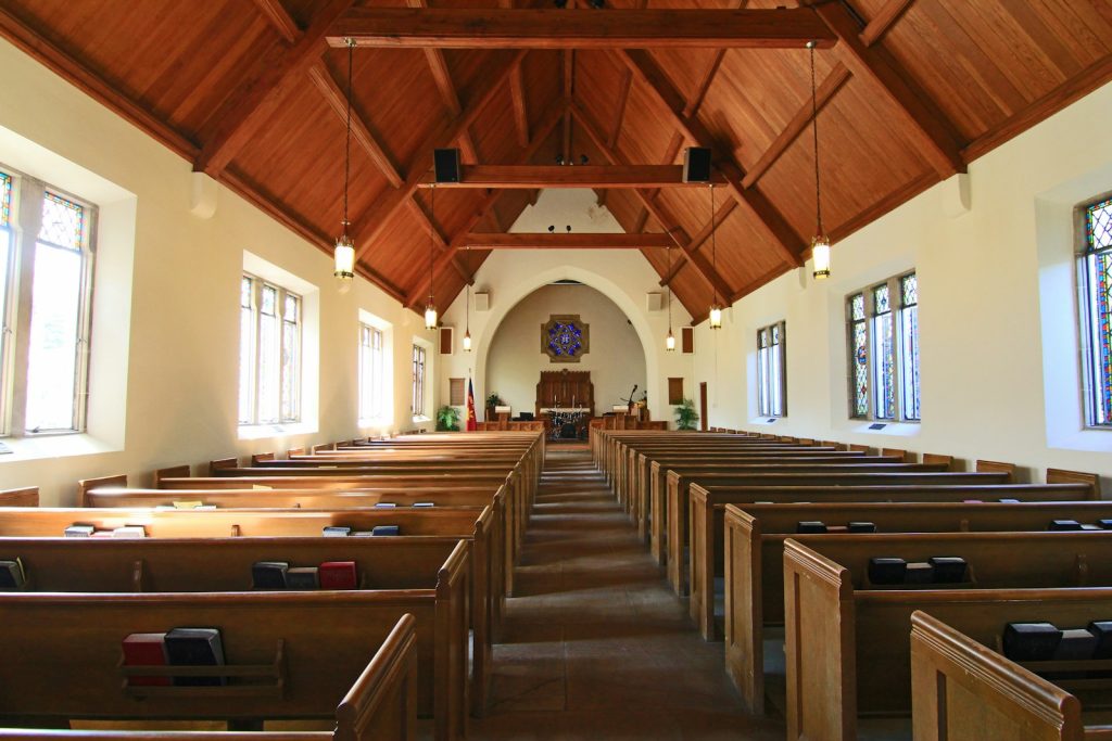Interior of a traditional church with wooden pews, stained glass windows, and a vaulted wooden ceiling