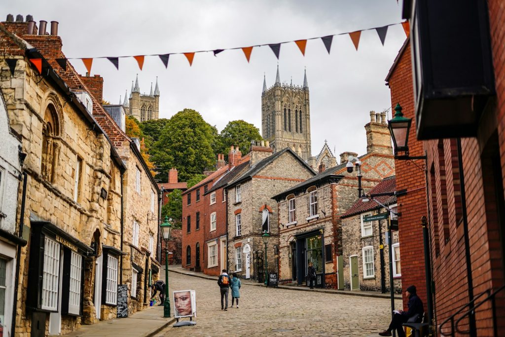 Historic street view with cottages leading to cathedral towers in Lincoln, UK, under a cloudy sky and bunting decorations