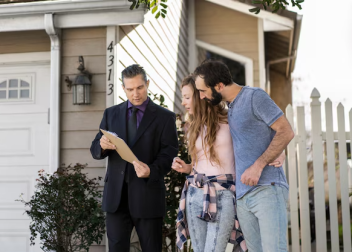 Real estate agent showing a couple a house listing outside a modern home