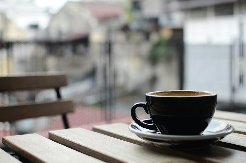 Black coffee cup on wooden table in an outdoor cafe setting with blurred background