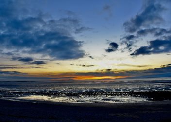 Coastal sunset with dramatic clouds and reflecting tide in Norfolk, UK, highlighting serene twilight atmosphere