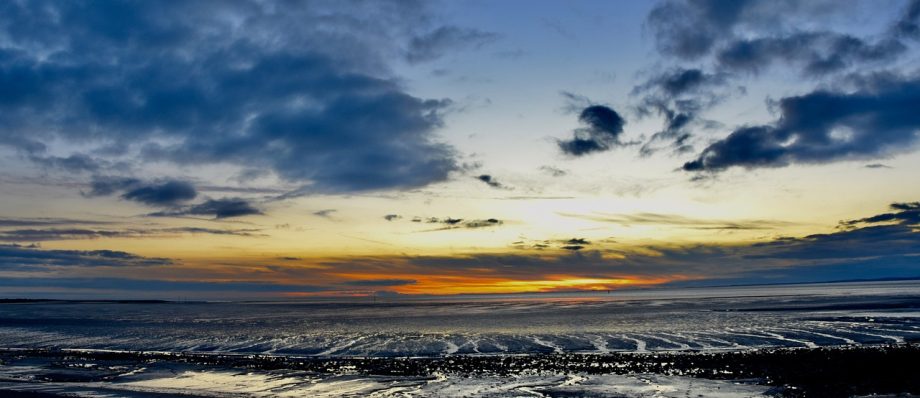 Coastal sunset with dramatic clouds and reflecting tide in Norfolk, UK, highlighting serene twilight atmosphere