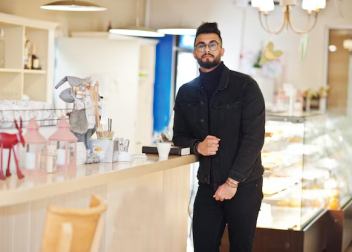 Man in a black jacket standing by a cafe counter, surrounded by cosy decor and soft lighting