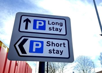 Parking sign indicating directions for long stay and short stay options, set against a blue sky background