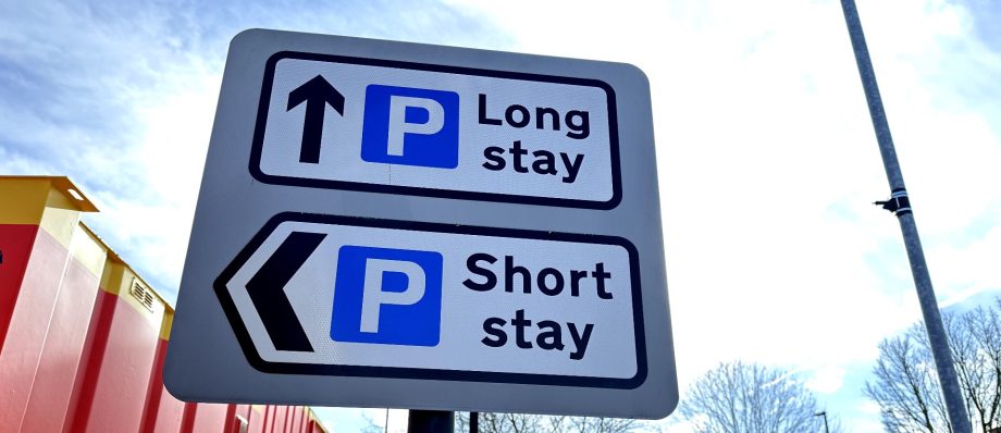 Parking sign indicating directions for long stay and short stay options, set against a blue sky background