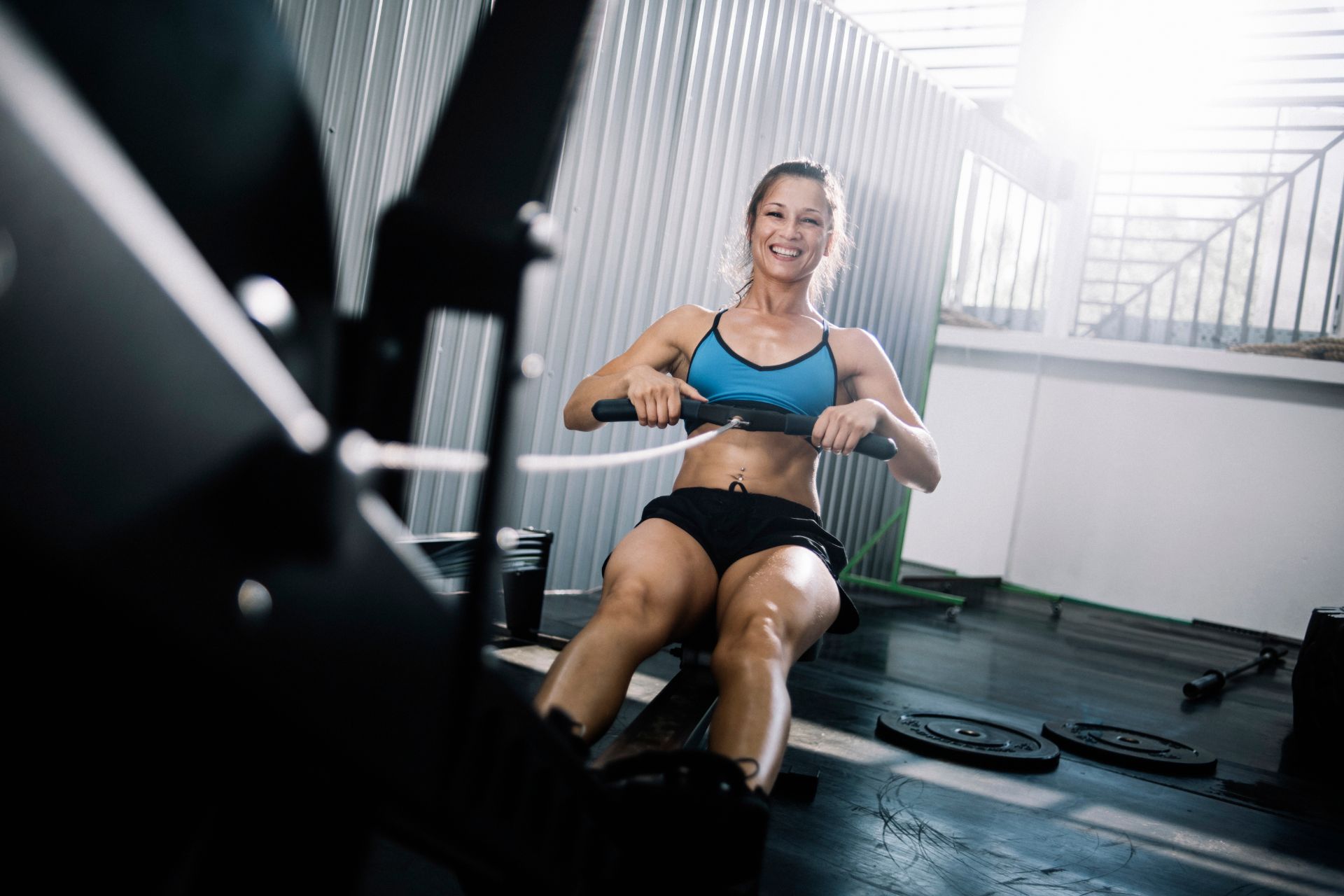 A woman is seated on a rowing machine, focusing on her workout in a bright, well-lit gym environment