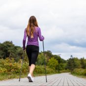 woman with walking sticks walks along a scenic path lined with trees