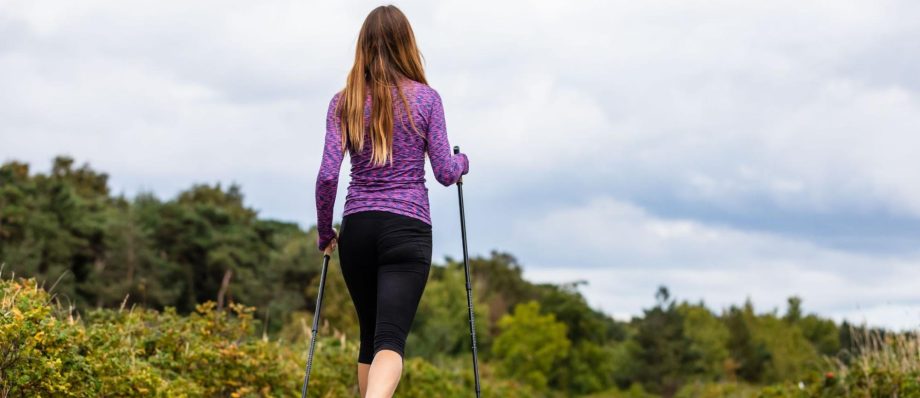 woman with walking sticks walks along a scenic path lined with trees