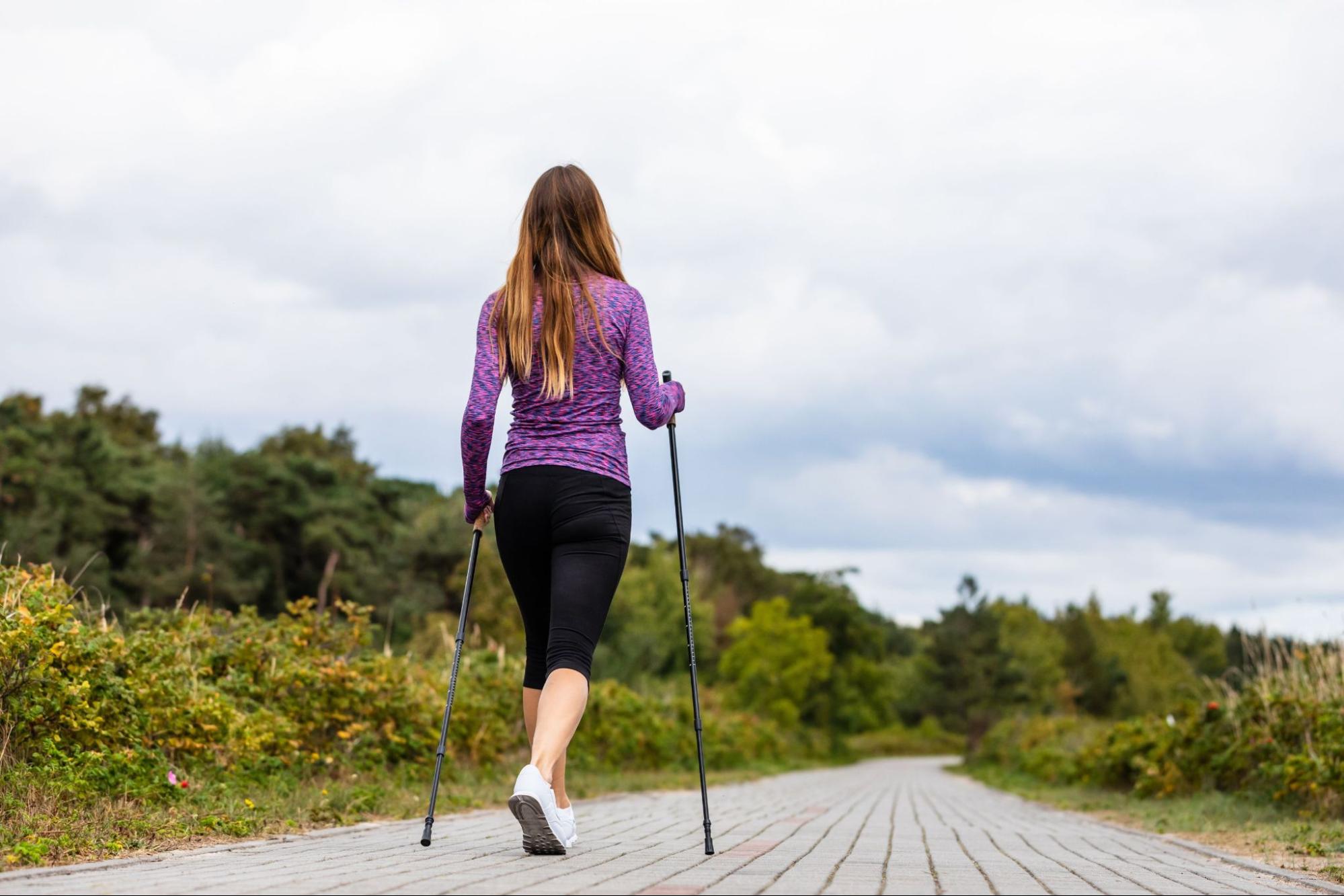 woman with walking sticks walks along a scenic path lined with trees