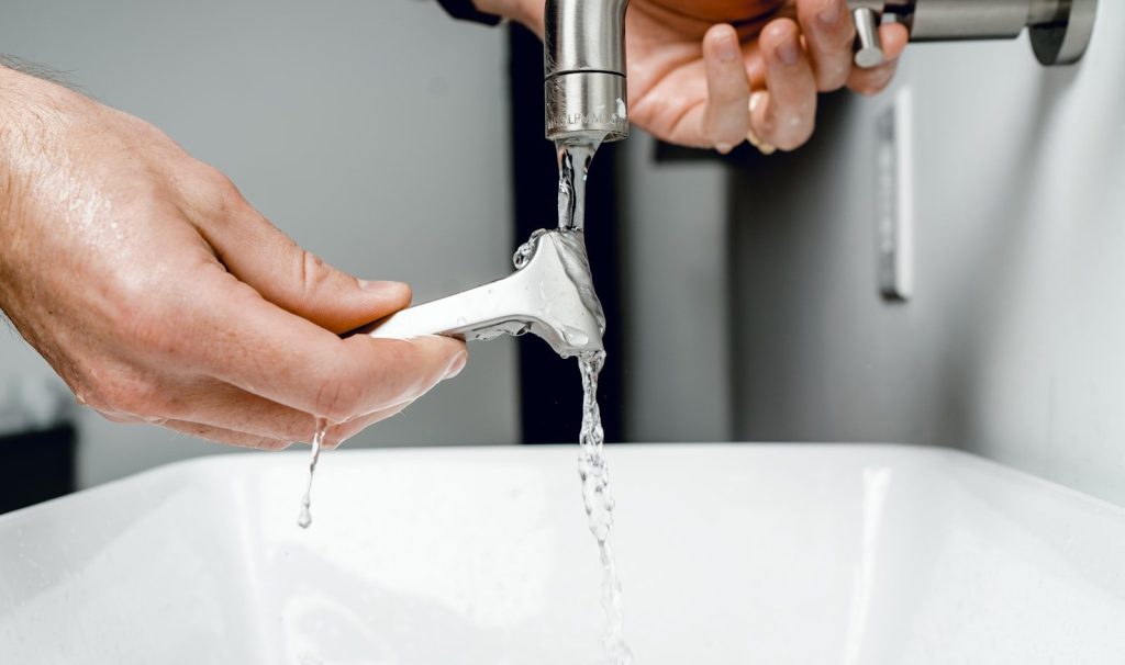 Man rinsing razor under tap water in modern bathroom sink