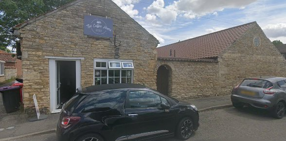 Stone building with parked black car, featuring The Coffee House sign under cloudy sky in a quaint village setting
