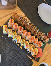 Assorted sushi rolls on a slate platter with colourful toppings and sauces on a wooden table setting