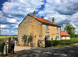 Charming countryside cottage with red roof, lush hedges, and dramatic sky in rural England landscape