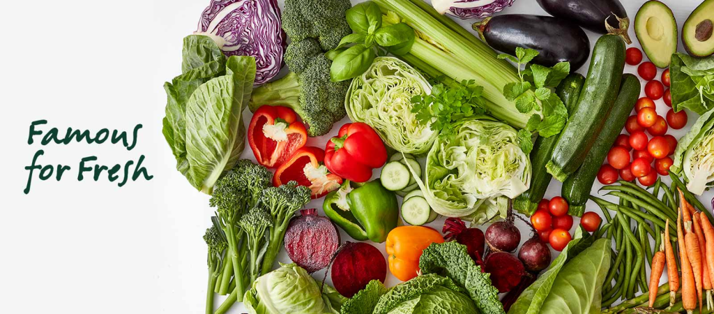 Assortment of fresh vegetables including lettuce, peppers, cucumbers, and carrots on a white background