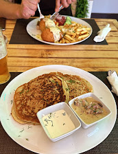 Plate with savoury pancakes, creamy sauces, person enjoying a fried dish with chips in the background