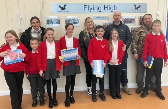 School children and teachers celebrating achievements under 'Flying High' sign, holding certificates and smiling
