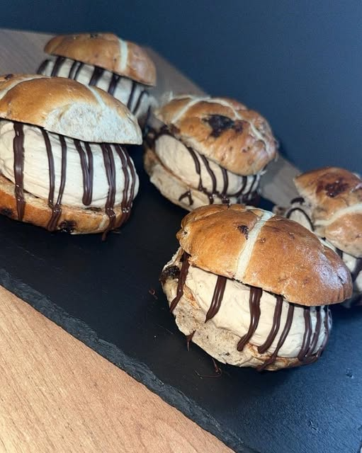 Delicious hot cross buns with creamy filling drizzled with chocolate on a slate platter