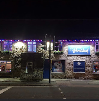 Stone pub at night with festive lights and signage for live sports, named Wheatsheaf on a quiet street in the UK