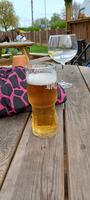 Pint of beer on wooden table outside in a pub garden with a patterned jacket and empty glass nearby