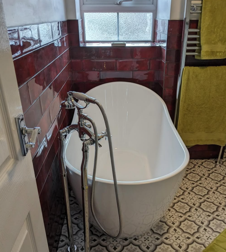 Freestanding bathtub with chrome tap in stylish red-tiled bathroom and patterned floor tiles