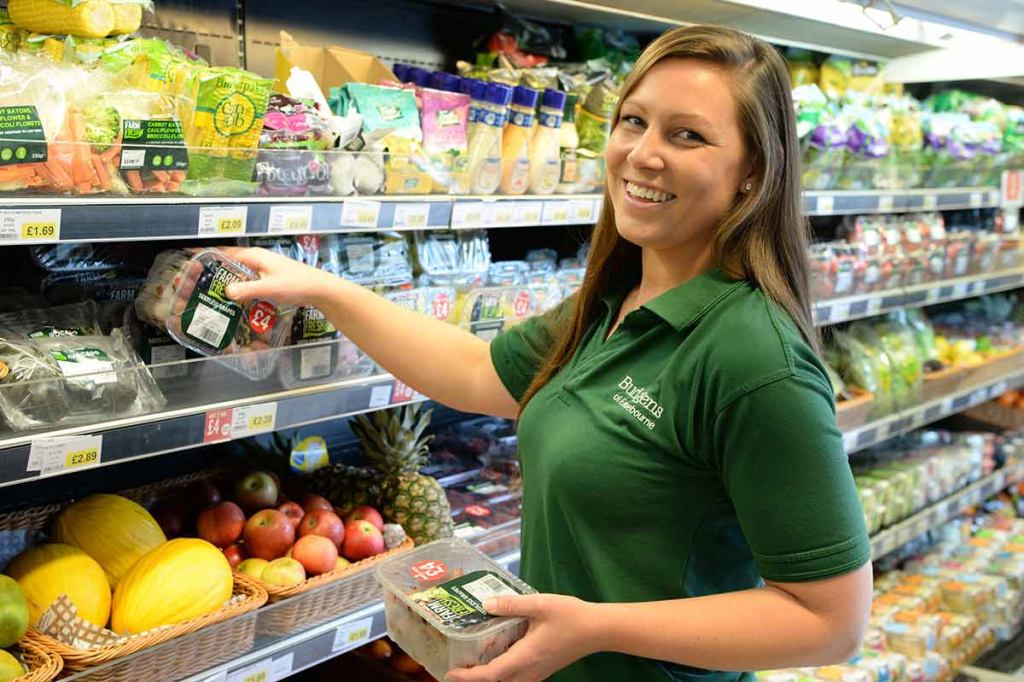 Supermarket employee stocking fresh produce in grocery aisle with a smile