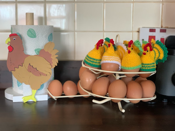Egg holder with knitted chicken covers alongside a rooster-themed kitchen towel holder on counter