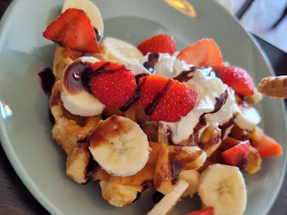Plate of waffles topped with fresh strawberries, bananas, whipped cream, and chocolate drizzle, served on a light blue plate