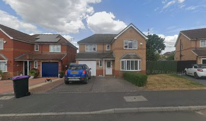 Suburban brick house with blue car parked in driveway, surrounded by similar homes under a cloudy blue sky
