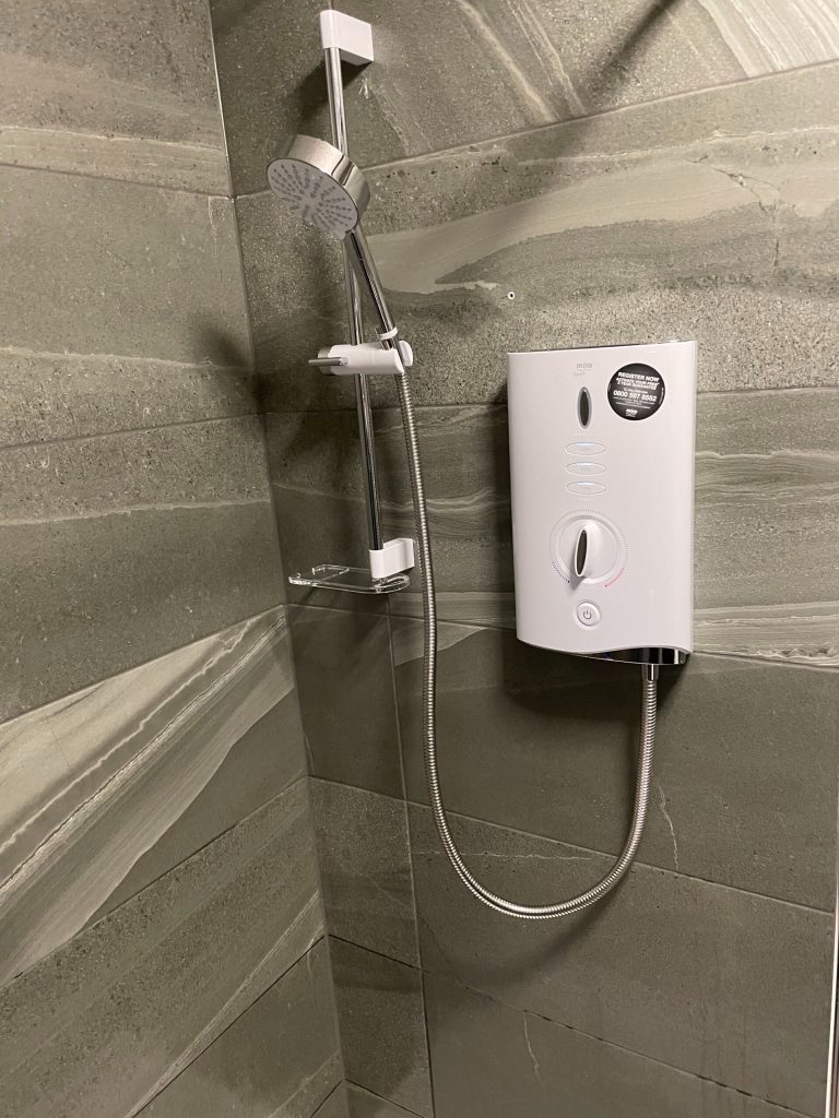 Modern shower unit installed on grey tiled bathroom wall with adjustable showerhead and sleek design