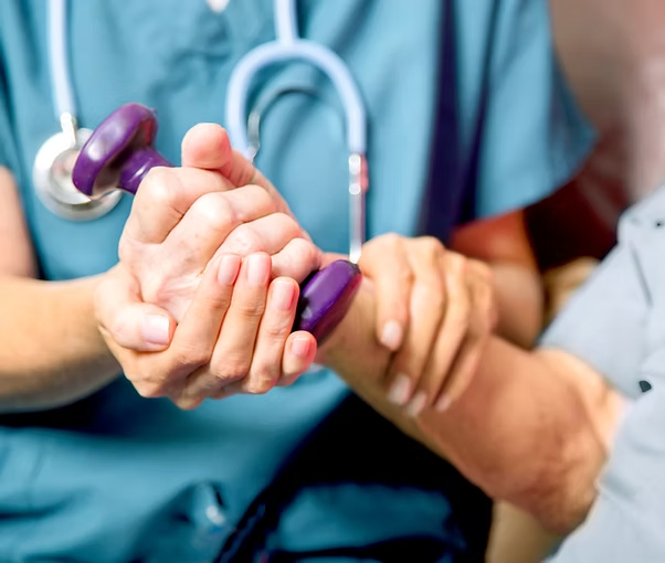 Elderly patient receiving physiotherapy with dumbbell support from healthcare professional in blue scrubs and stethoscope