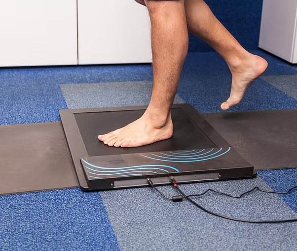 Person stepping on digital foot scanner for gait analysis on blue carpeted floor in office setting