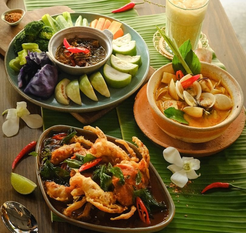Assorted Thai dishes with fresh vegetables, seafood soup, crab dish and herbal drink on banana leaf setting