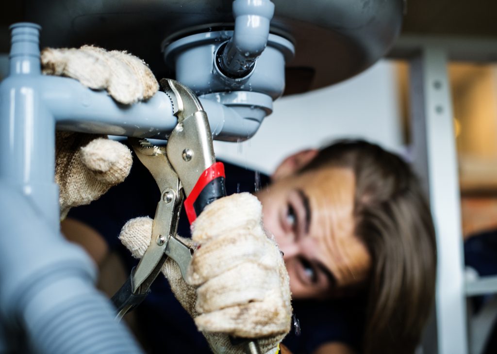 Plumber repairing sink pipe with pliers, focused on fixing leak, wearing protective gloves, home maintenance task